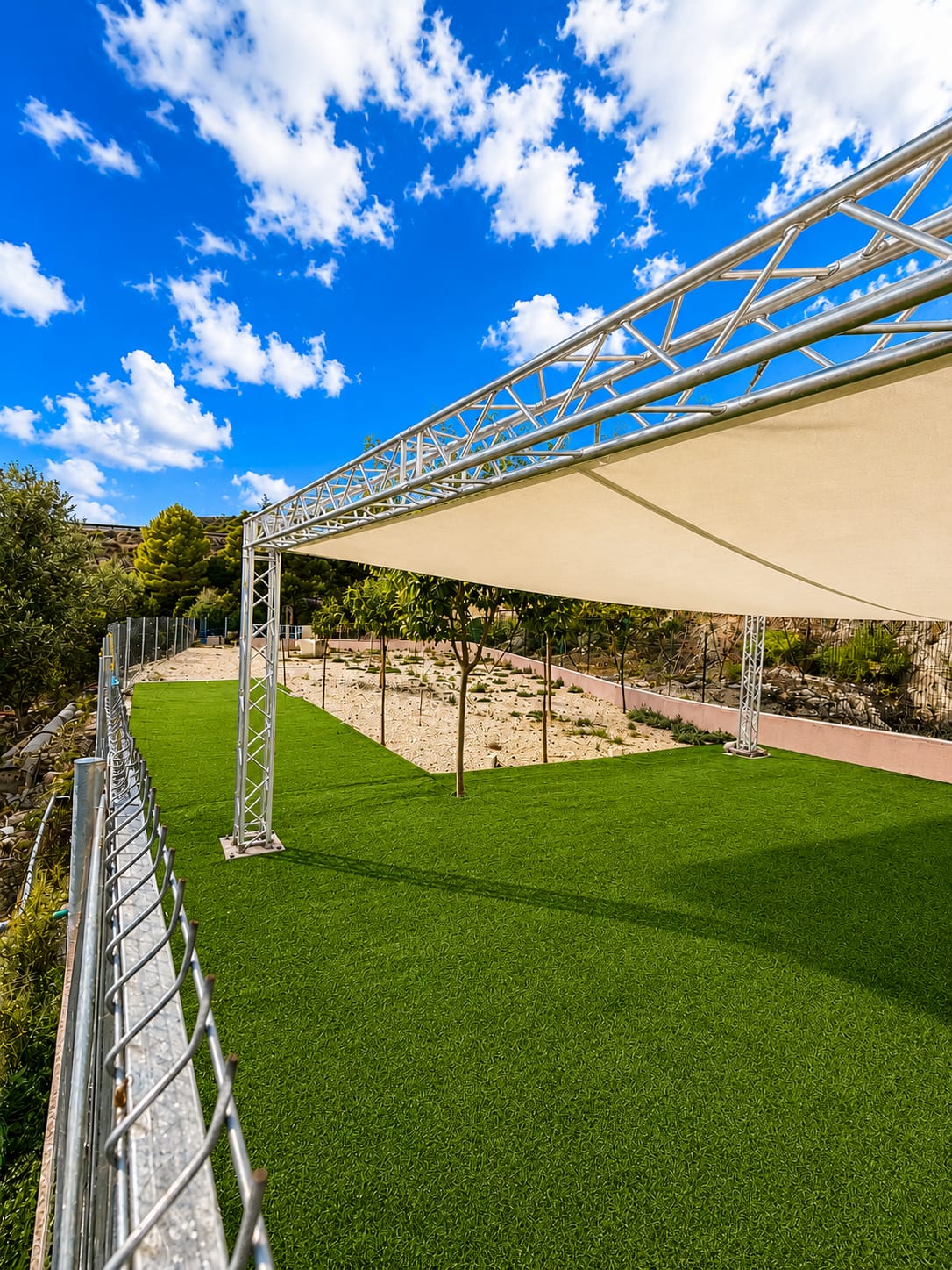 Zona de césped con estructura de sombra y pinos al fondo